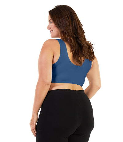 Plus size woman, facing back, wearing JunoActive plus size Stretch Naturals Scoop Neck Bra in french blue. The woman is wearing black plus size JunoActive leggings. Her arms fall naturally to her side.