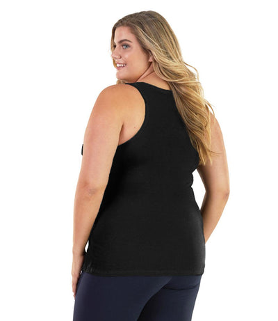 Plus size woman, facing back, wearing JunoActive plus size Stretch Naturals Tank in Black. The woman is wearing a pair of Navy Blue JunoActive leggings.