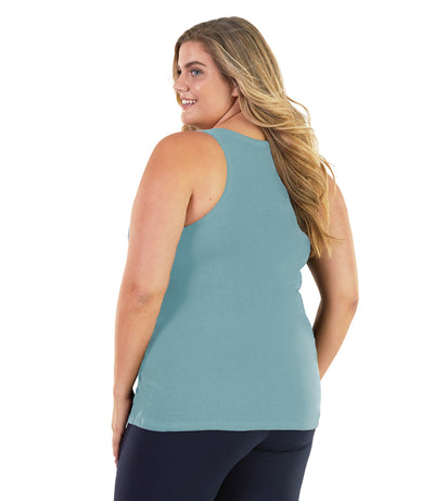 Plus size woman, facing back, wearing JunoActive plus size Stretch Naturals Tank in Soft Green. The woman is wearing a pair of Navy Blue JunoActive leggings. 