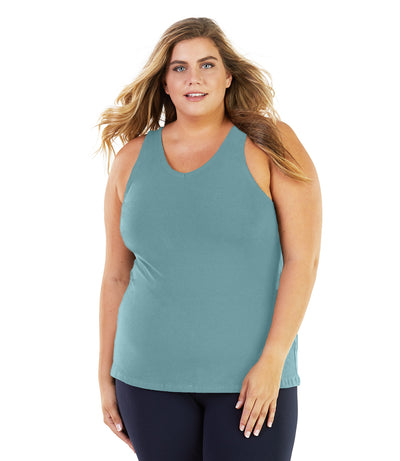 Plus size woman, facing front, wearing JunoActive plus size Stretch Naturals Tank in Soft Green. The woman is wearing a pair of Navy Blue JunoActive leggings. 