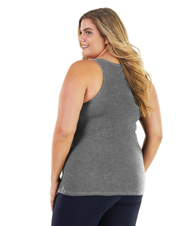 Plus size woman, facing back, wearing JunoActive plus size Stretch Naturals Tank in Heather Grey. The woman is wearing a pair of Navy Blue JunoActive leggings. 