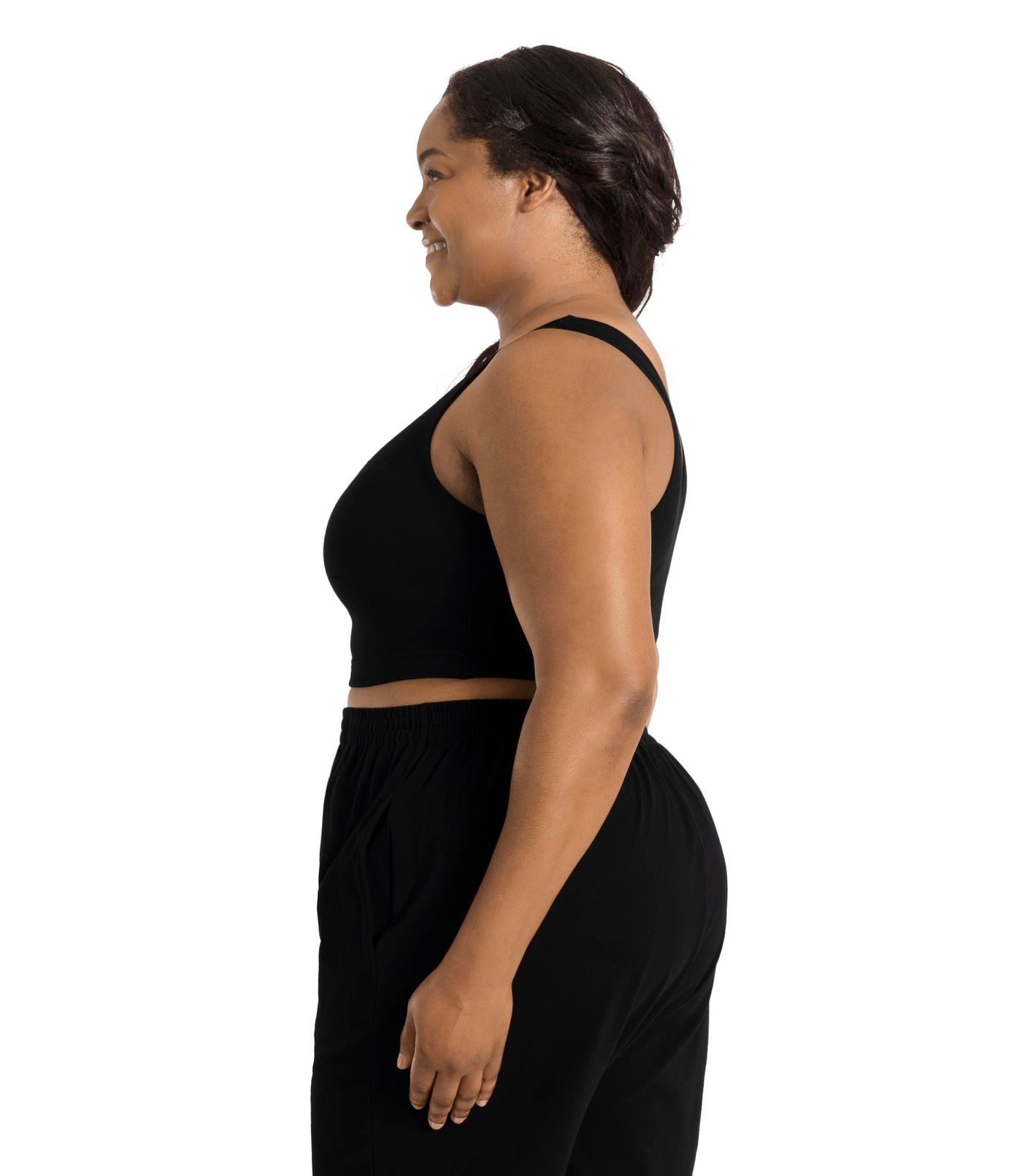 Plus size woman, facing side profile, wearing JunoActive plus size Stretch Naturals Scoop Neck Bra in black. The woman is wearing black JunoActive plus size bottoms. Her arms fall naturally to her side.