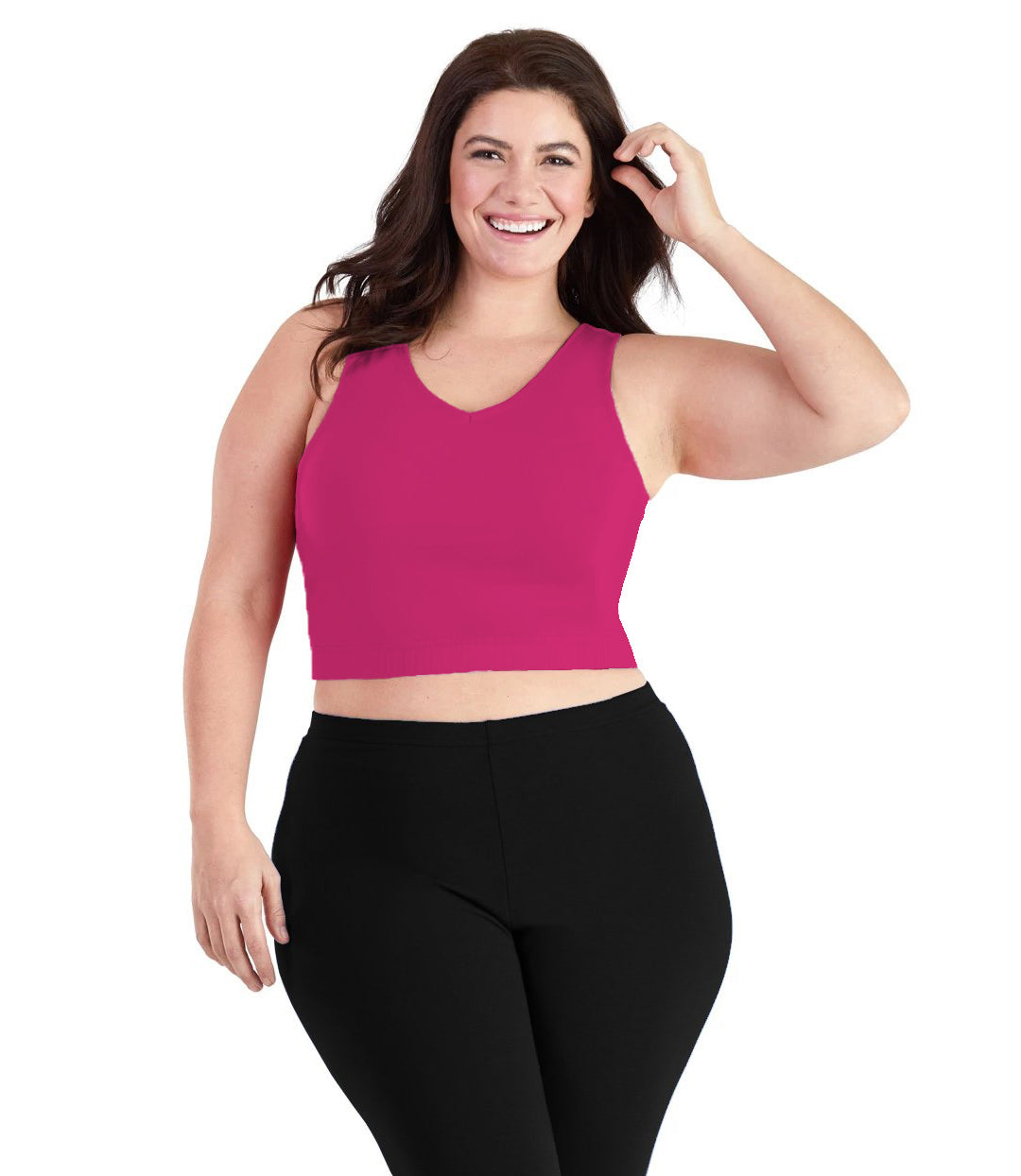Plus size woman, facing front, wearing JunoActive plus size Stretch Naturals V-Neck Bra top in Geranium Pink. The woman is wearing black JunoActive plus size leggings. Her left arm is tucking her hair behind her ear, her right arm falls naturally to her side. 