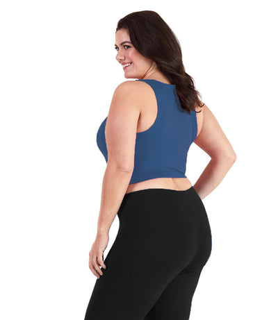Plus size woman, facing back, wearing JunoActive plus size Stretch Naturals V-Neck Bra top in French Blue. The woman is wearing black JunoActive plus size leggings. Her arms fall naturally to her side.