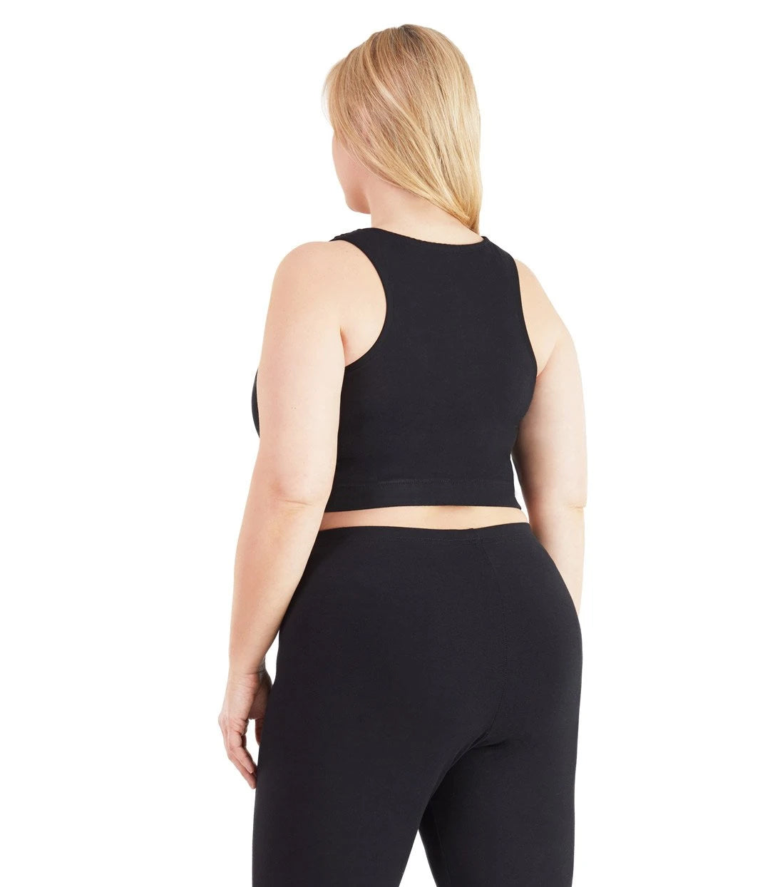 Plus size woman, facing back, wearing JunoActive plus size Stretch Naturals V-Neck Bra top in black. The woman is wearing black JunoActive plus size leggings. Her arms fall naturally to her side.