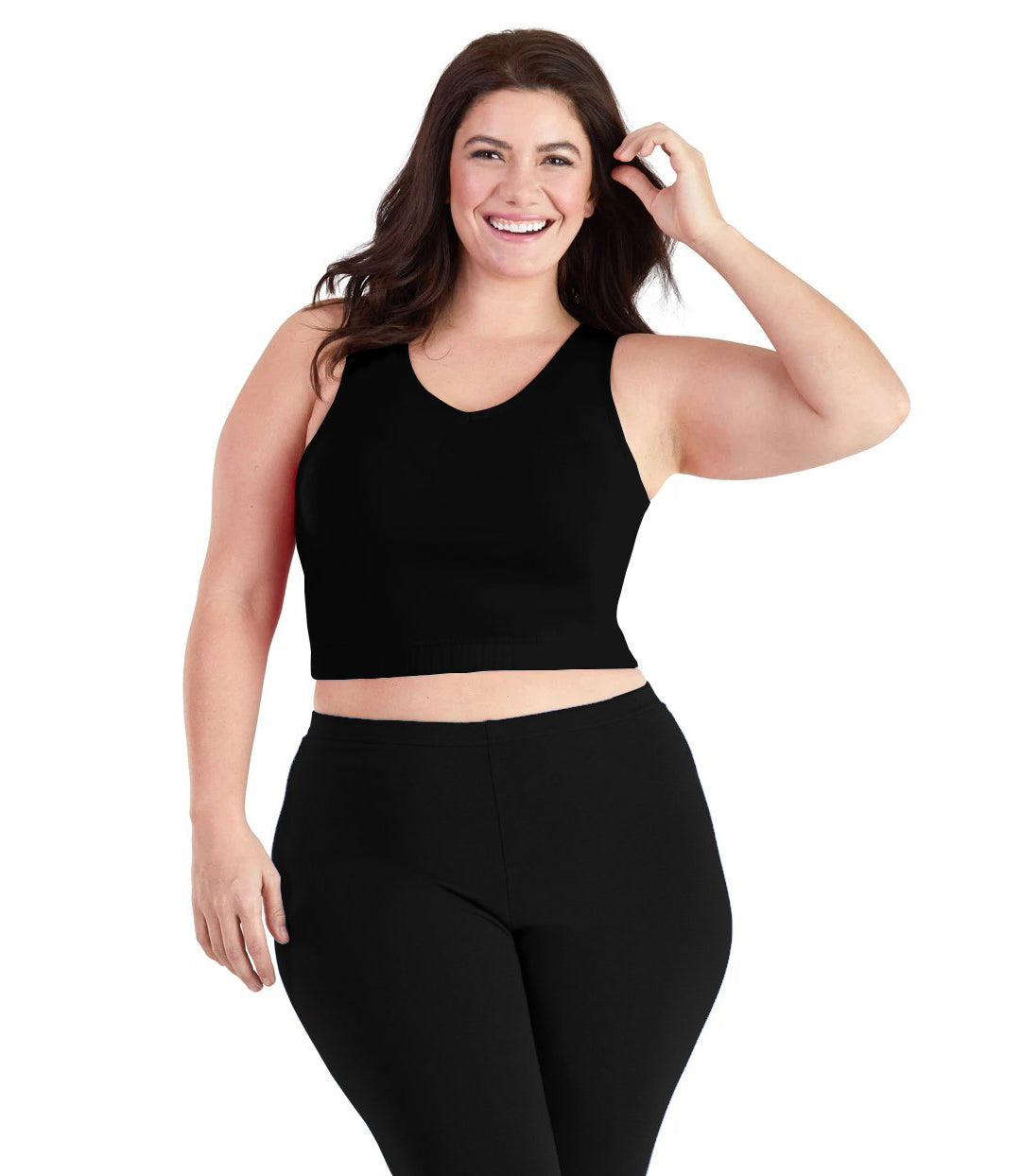 Plus size woman, facing front, wearing JunoActive plus size Stretch Naturals V-Neck Bra top in black. The woman is wearing black JunoActive plus size leggings. Her left arm is up tucking her hair behind her ear, her right arm falls naturally to her side. 