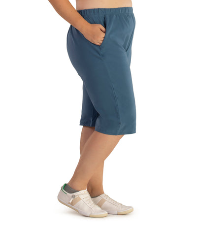 Bottom half of plus sized woman, side view, wearing JunoActive Stretch Naturals Bermuda Shorts in color denim blue. Bottom hem is at the knee.