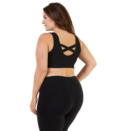 Plus size woman, facing back, wearing JunoActive plus size Stretch Naturals Crossback Bra Top in Black. The woman is wearing a pair of Black JunoActive fitted boxers. 