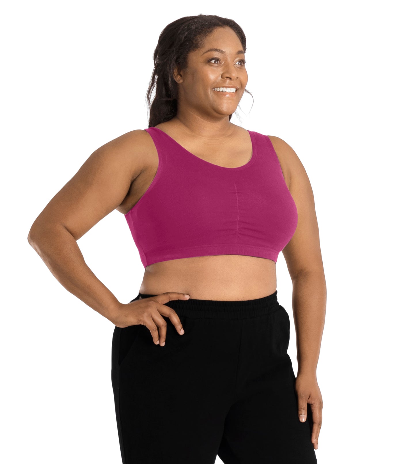 Plus size woman, facing to the side, looking away, right hand on hip, left hand by side, wearing JunoActive Stretch Naturals Shirred Bra Top. Bra is gathered in middle and is a scoop top neck. Straps are wide and bra color is merlot.