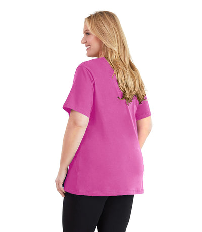 Plus size woman, facing back and looking left, wearing JunoActive plus size Stretch Naturals V-Neck in the color Lovely Pink. She is wearing JunoActive Plus Size Leggings in the color black.