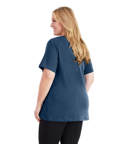 Plus size woman, facing back and looking left, wearing JunoActive plus size Stretch Naturals V-Neck in the color Denim Blue. She is wearing JunoActive Plus Size Leggings in the color black.