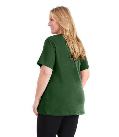 Plus size woman, facing back and looking left, wearing JunoActive plus size Stretch Naturals V-Neck in the color Evergreen. She is wearing JunoActive Plus Size Leggings in the color black.
