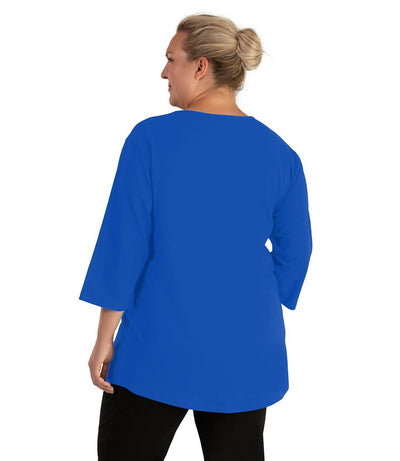 Plus size woman, facing back looking left, wearing JunoActive plus size Stretch Naturals Scoop Neck ¾ Sleeve Top in the color Vivid Blue. She is wearing JunoActive Plus Size Leggings in the color Black.