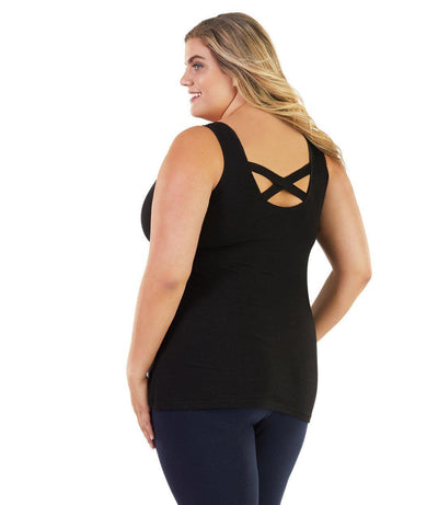Plus size woman, facing back, wearing JunoActive plus size Stretch Naturals Crossback Tank in Black. The woman is wearing a pair of Navy Blue JunoActive fitted leggings.