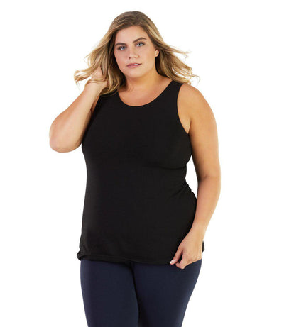 Plus size woman, facing front, wearing JunoActive plus size Stretch Naturals Crossback Tank in Black. The woman is wearing a pair of Navy Blue JunoActive fitted leggings.