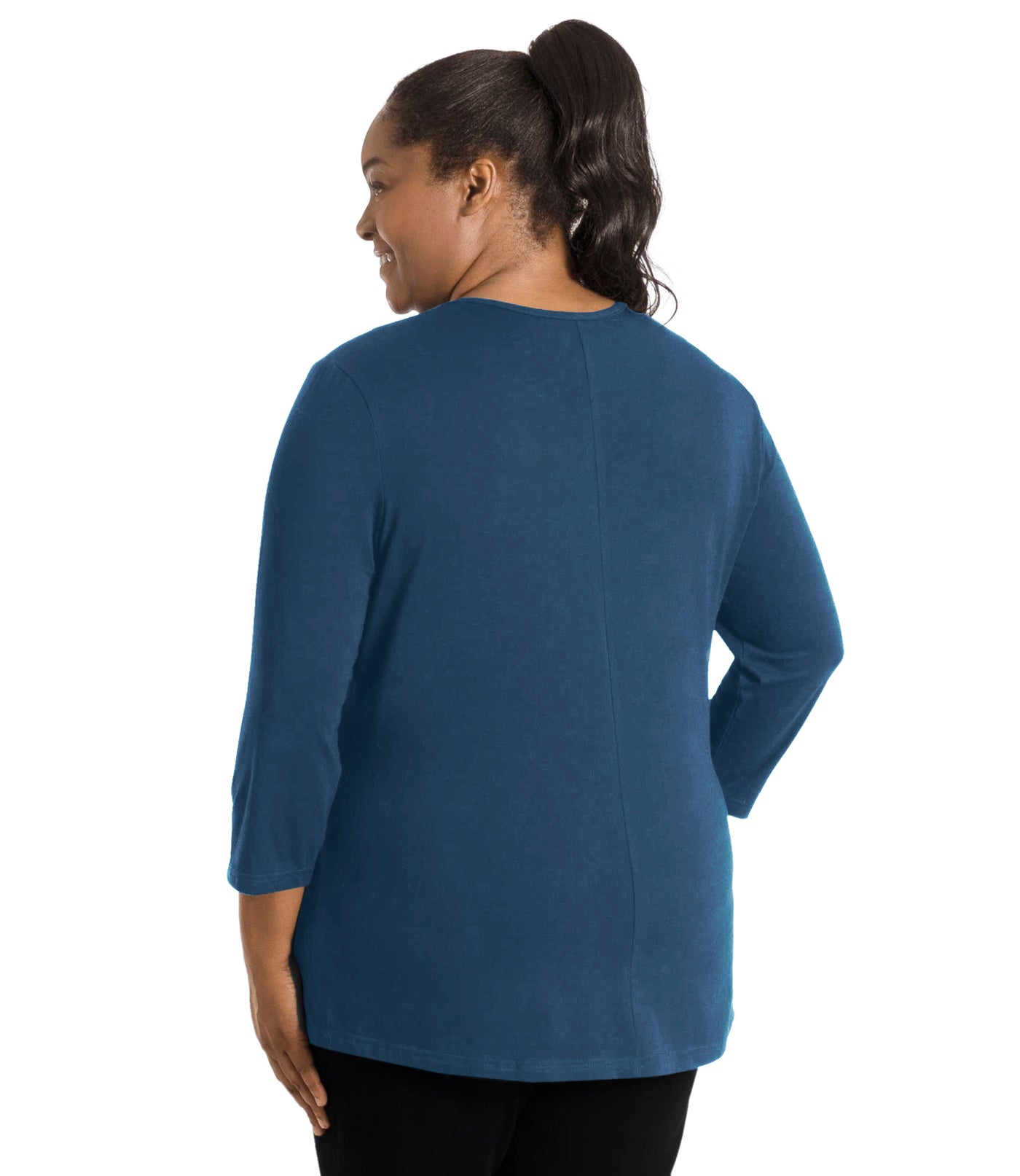 Plus size woman, facing back, wearing JunoActive’s Stretch Naturals Center Seam Scoop Neck 3/4 sleeve top in color denim blue. Hands are by side. Pants are in color black. 