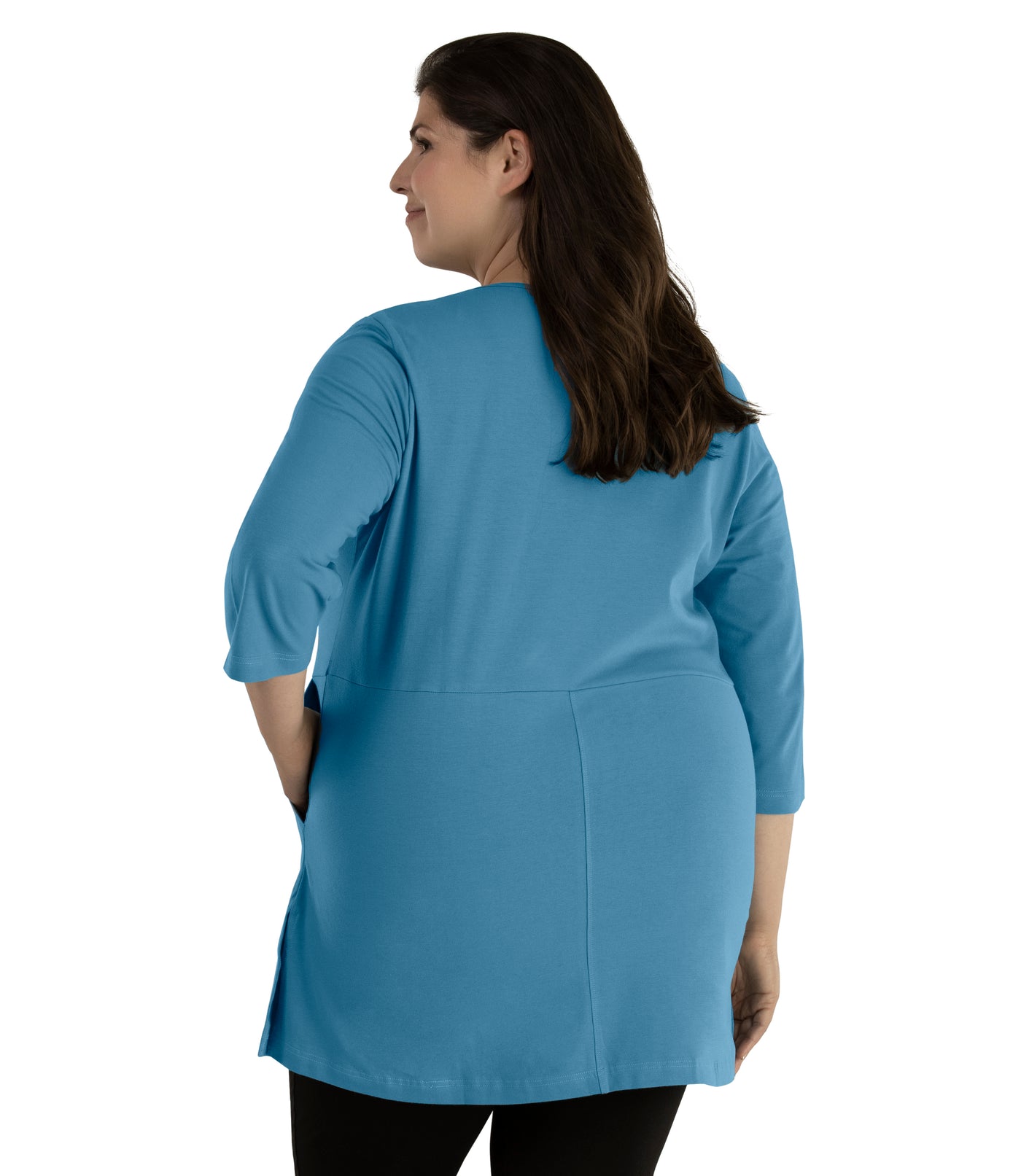 Plus size woman, facing back, wearing JunoActive plus size Stretch Naturals Empire Tunic with Pockets in the color Dusty Teal. Her left hand is in the tunic pocket at her waist level. She is wearing JunoActive Plus Size Leggings in the color Black.