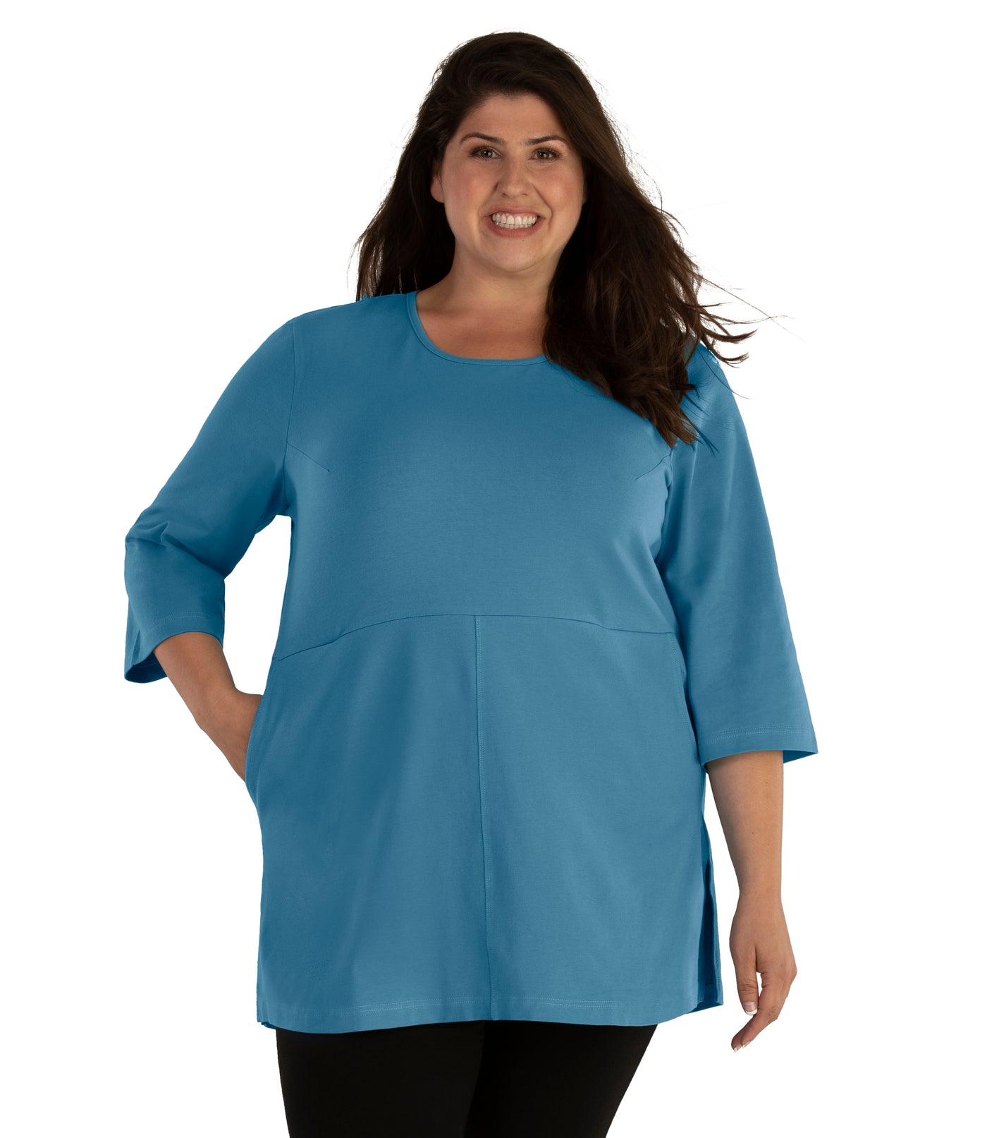 Plus size woman, facing front, wearing JunoActive plus size Stretch Naturals Empire Tunic with Pockets in the color Dusty Teal. Her left hand is in the tunic pocket at her waist level. She is wearing JunoActive Plus Size Leggings in the color Black.
