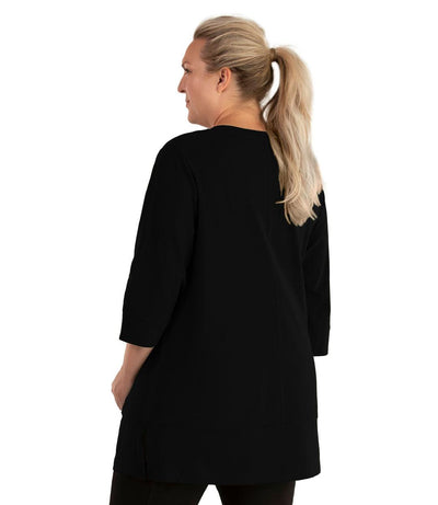 Plus size woman, facing back looking left, wearing JunoActive plus size Stretch Naturals Princess V-neck Tunic in the color Black. She is wearing JunoActive Plus Size Leggings in the color Black