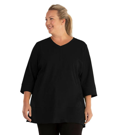 Plus size woman, facing front, wearing JunoActive plus size Stretch Naturals Princess V-neck Tunic in the color Black. She is wearing JunoActive Plus Size Leggings in the color Black.
