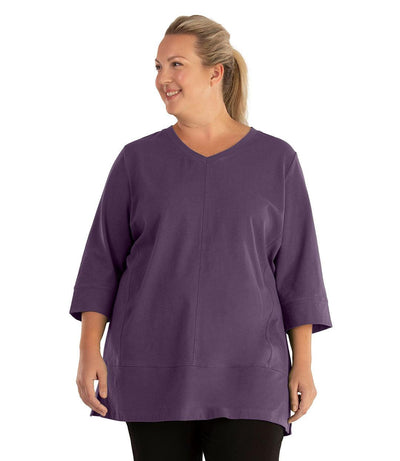 Plus size woman, facing front, wearing JunoActive plus size Stretch Naturals Princess V-neck Tunic in the color Blackberry. She is wearing JunoActive Plus Size Leggings in the color Black.