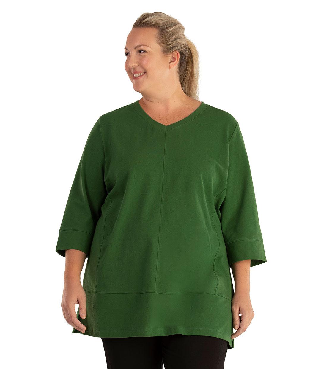 Plus size woman, facing front, wearing JunoActive plus size Stretch Naturals Princess V-neck Tunic in the color Evergreen. She is wearing JunoActive Plus Size Leggings in the color Black.