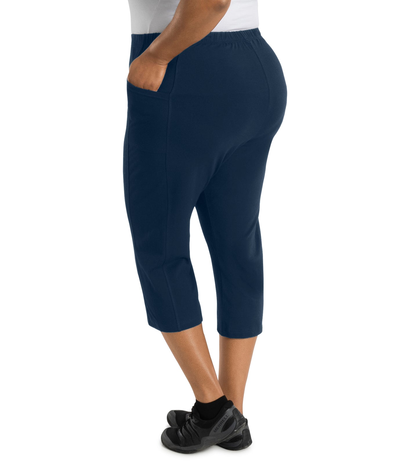 Bottom half of plus size woman facing sideways left hand in pocket, wearing JunoActive Stretch Naturals side pocket capri pant bottom. The hemline comes to mid-calf and hugs the body without being skin tight. Color is indigo.