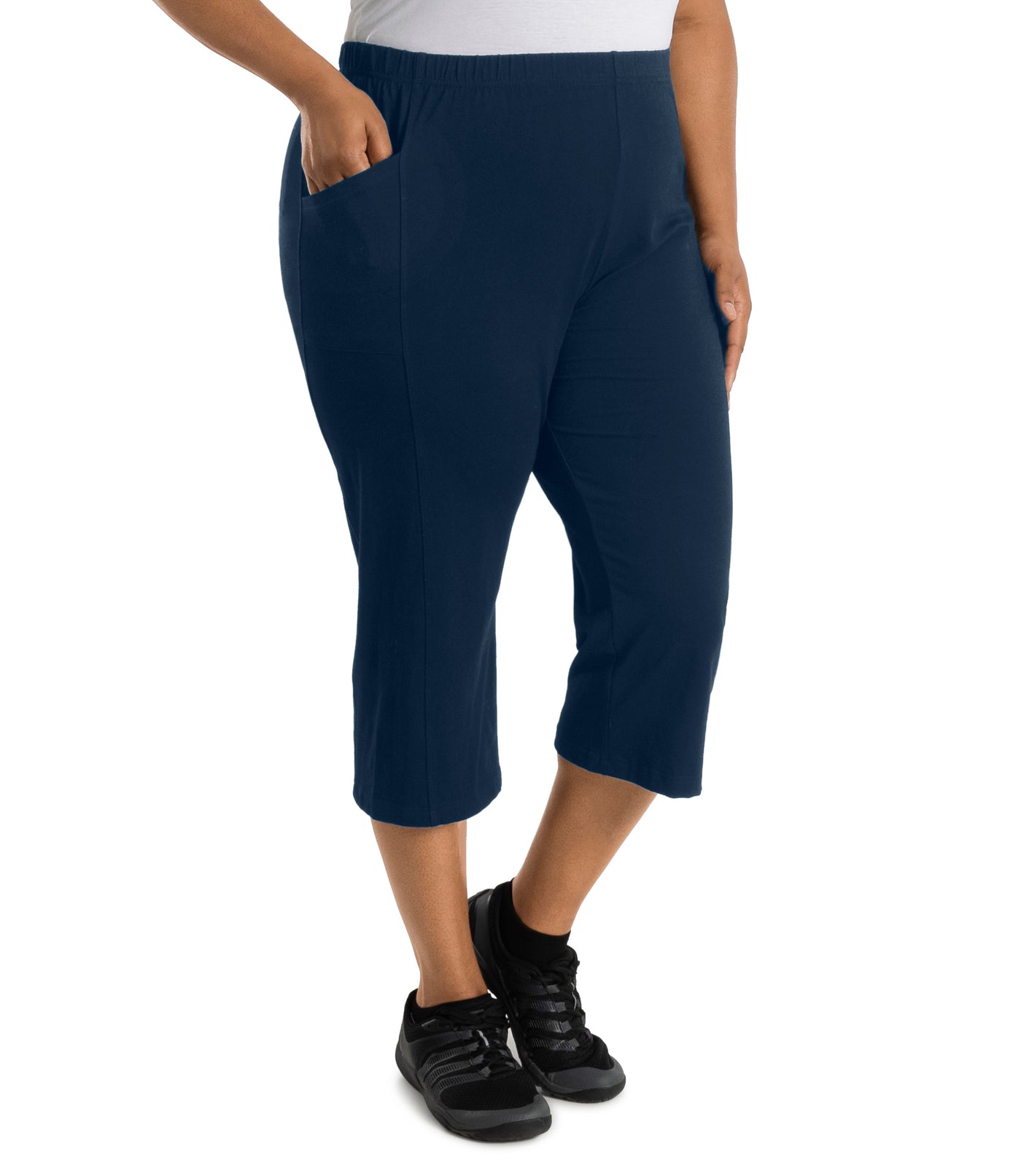 Plus size woman is facing at a side angle, right hand in pocket, left arm and hand to side, wearing JunoActive Stretch Naturals side pocket capri pant bottom. The hemline comes to mid-calf and hugs the body without being skin tight. Color is indigo.