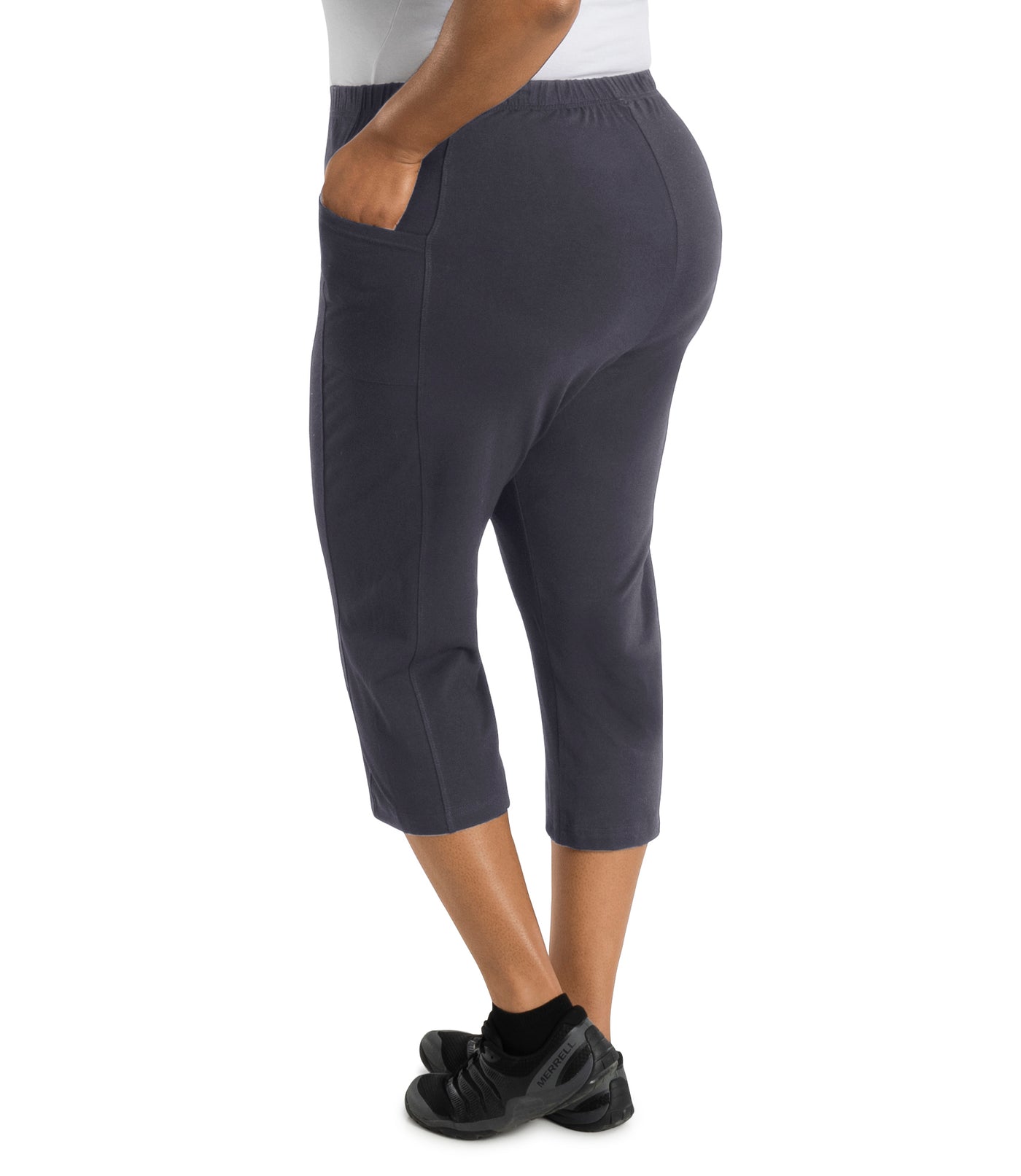 Plus size woman facing towards back, left hand in pocket, wearing JunoActive Stretch Naturals side pocket plus size capri pant bottom. The hemline comes to mid-calf and hugs the body without being skin tight. Color is oak gray.