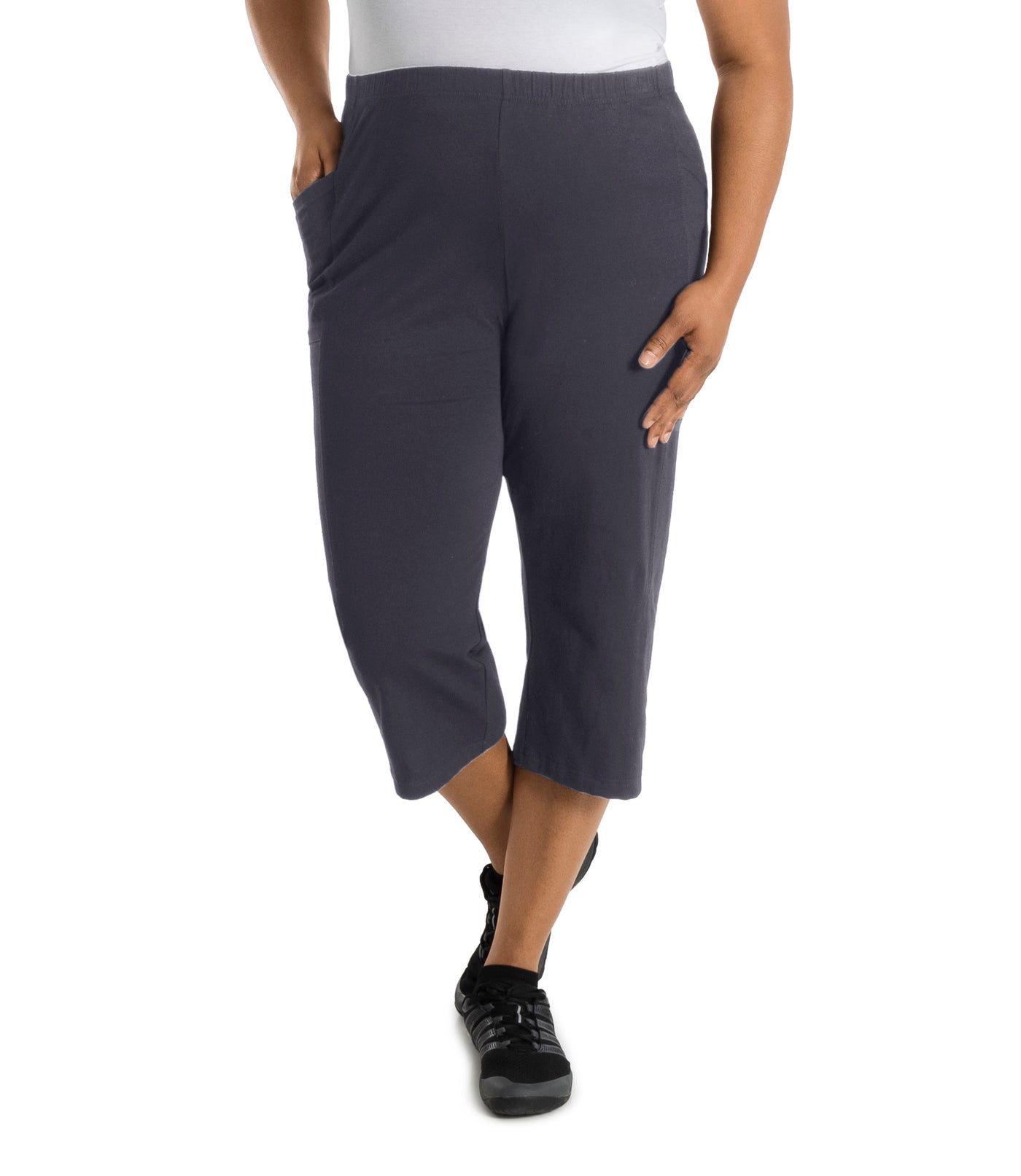 Plus size woman is facing forward, right hand in pocket, left arm and hand to side, wearing JunoActive Stretch Naturals side pocket plus size capri pant bottom. The hemline comes to mid-calf and hugs the body without being skin tight. Color is oak gray.