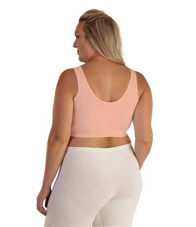 Plus size woman, facing back, wearing JunoActive plus size Junowear Hush V-Neck Bra in Peach. The woman is wearing a white Junowear Hush Boxer brief. Her arms fall naturally to her side.