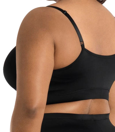 Plus size model wearing JunoActive's Junowear Hush adjustable bralette in color black. Models hands are by her side and she's facing back close up.