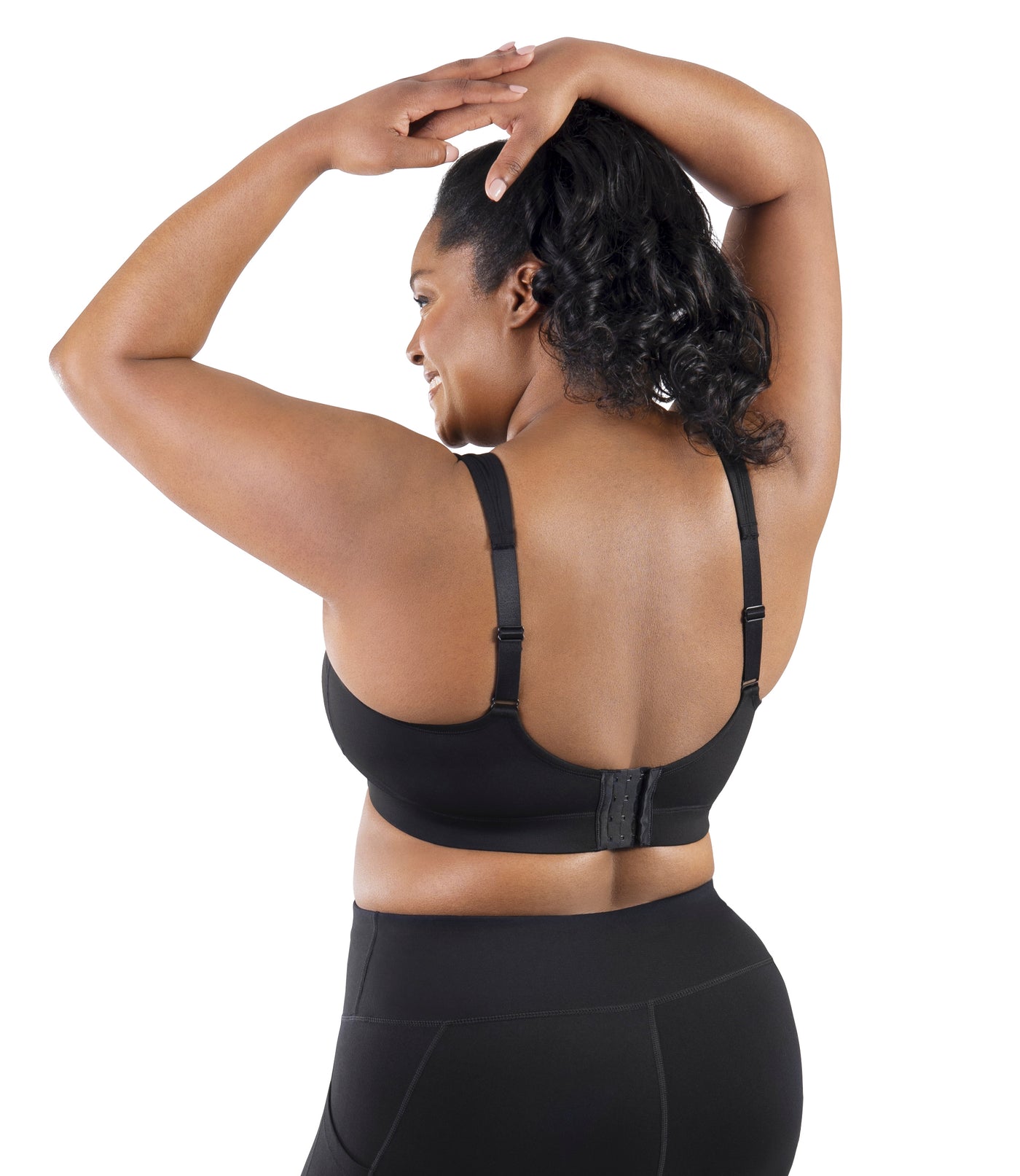 Comfort Support Back Clasp Sports Bra on model facing back in color black. Hands on top of head.