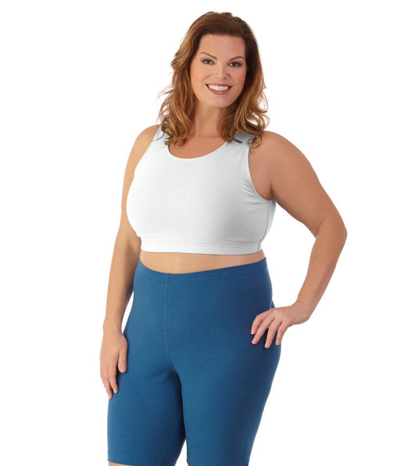 Plus size woman, facing front, wearing JunoActive plus size Stretch Naturals Scoop Neck Bra in white. The woman is wearing blue plus size JunoActive bike shorts. Her right arm falls naturally to her side, her left hand is on her hip. 