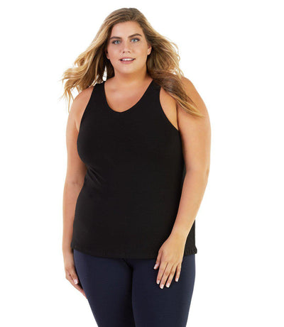 Plus size woman, facing front, wearing JunoActive plus size Stretch Naturals Tank in Black. The woman is wearing a pair of Navy Blue JunoActive leggings. 