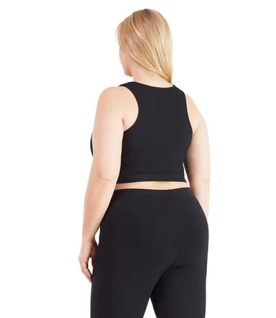 Plus size woman, facing back, wearing JunoActive plus size SupraKnit Long-Line V-Neck Bra top in Black. The woman is wearing black JunoActive plus size leggings.