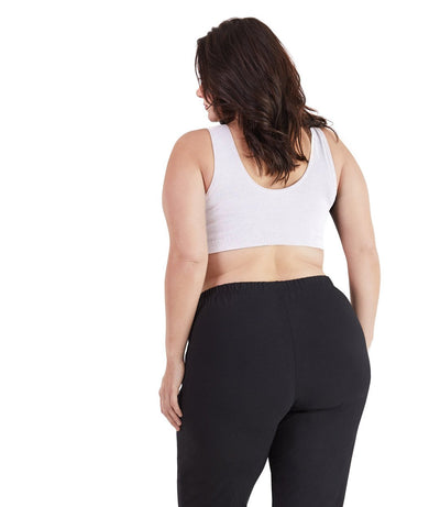 Plus size woman, facing back, wearing JunoActive plus size Stretch Naturals Scoop Neck Bra in white. The woman is wearing black JunoActive plus size leggings.  Her arms fall naturally to her side. 