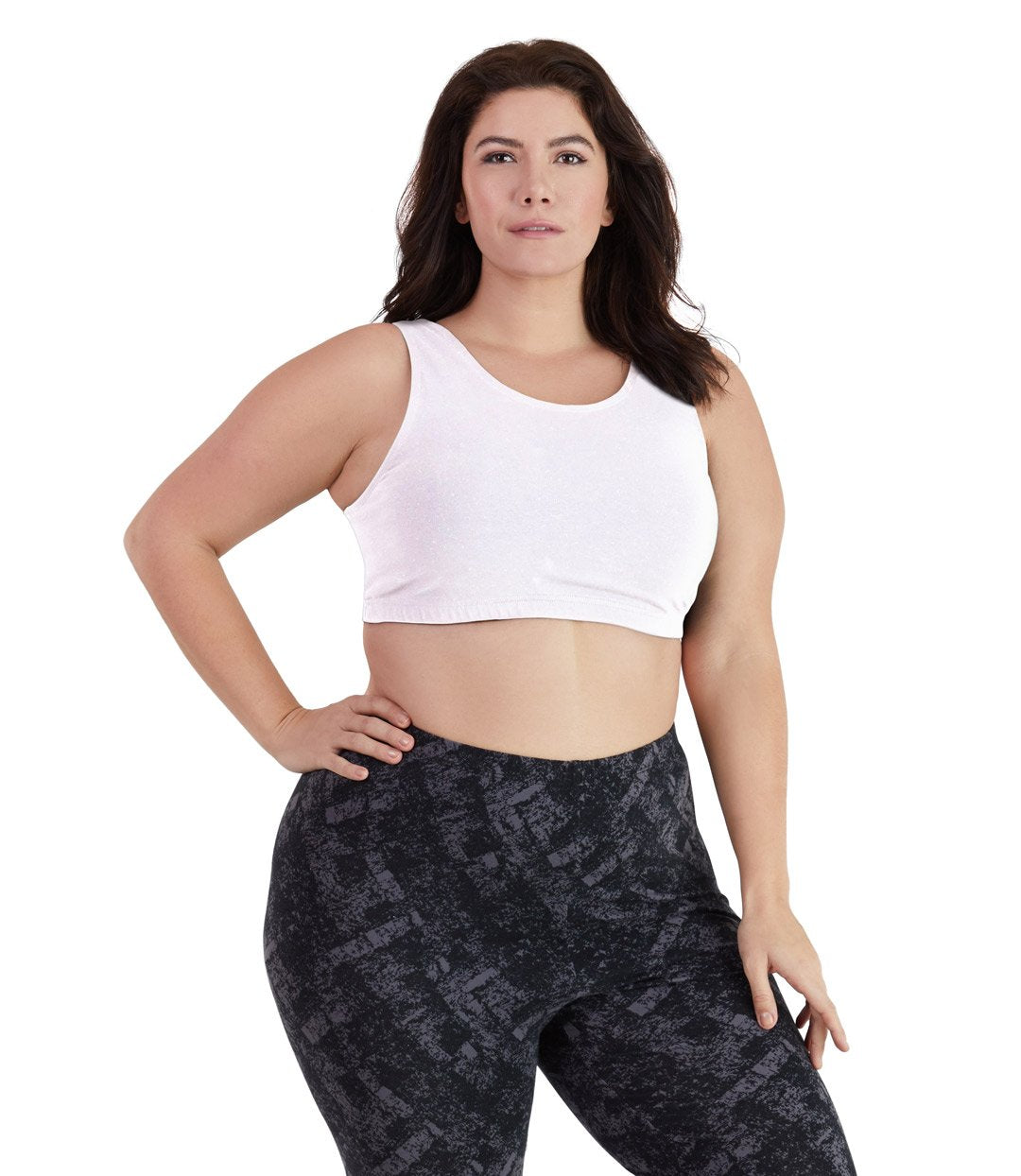 Plus size woman, facing front, wearing JunoActive plus size Stretch Naturals Scoop Neck Bra in white. The woman is wearing black JunoActive plus size leggings. Her right arm is on her hip, her left arm falls naturally to her side. 