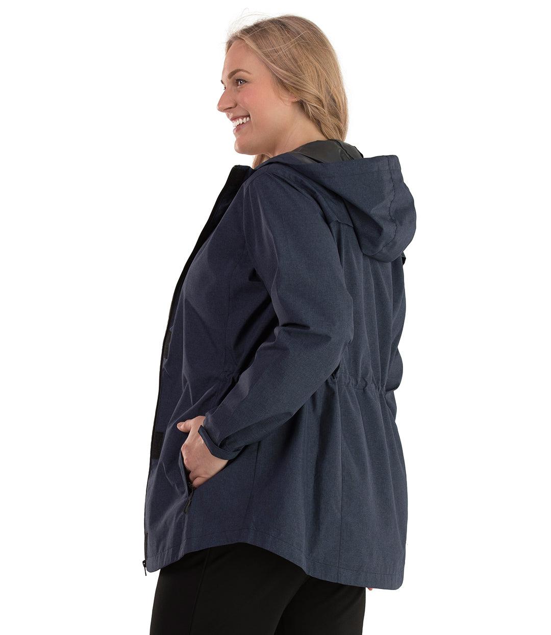 Plus size woman, side view, facing left wearing a JunoActive plus size Waterproof Breathable Wind & Rain Jacket in navy blue. The jacket has a hood, double front closure and side pockets. The length of the plus size jacket hits just below the hips.