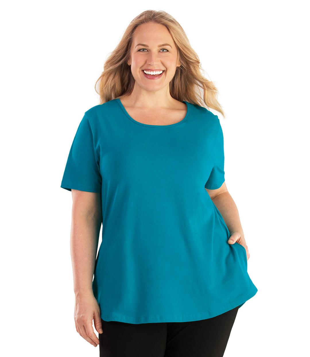 Plus size woman, facing front, wearing JunoActive plus size Stretch Naturals Lite Pocket Tee in the color Teal. Her right hand is in the shirt pocket by her hip, her left arm is naturally at her side. She is wearing JunoActive Plus Size Leggings in the color Black. 