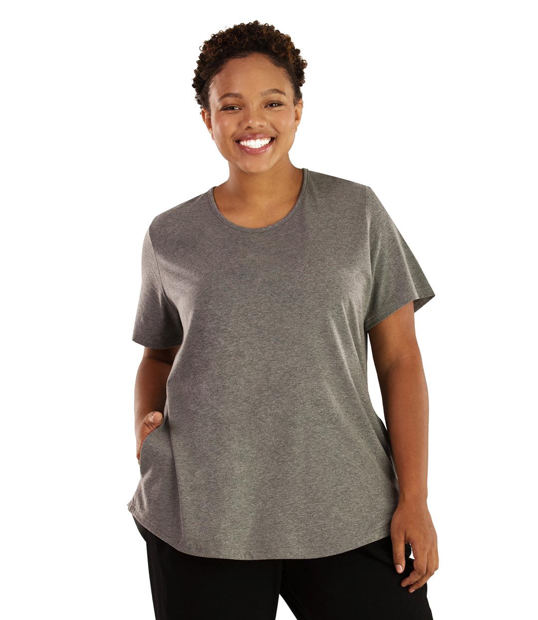 Plus size woman, facing front, wearing JunoActive plus size Stretch Naturals Lite Pocket Tee in the color Heather Grey. Her right hand is in the shirt pocket by her hip, her left arm is naturally at her side. She is wearing JunoActive Plus Size Leggings in the color Black. 