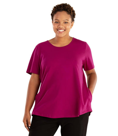 Plus size woman, facing front, wearing JunoActive plus size Stretch Naturals Lite Pocket Tee in the color Magenta. Her right hand is in the shirt pocket by her hip, her left arm is naturally at her side. She is wearing JunoActive Plus Size Leggings in the color Black. 