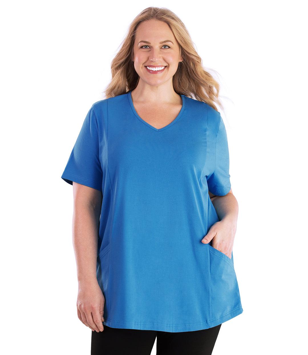 Plus size woman, facing front, wearing JunoActive plus size Stretch Naturals Lite Pocketed V-Neck Short Sleeve Top in the color Dutch Blue. Her left hand is in the shirt pocket by her hip, her right arm is naturally at her side. She is wearing JunoActive Plus Size Leggings in the color Black.