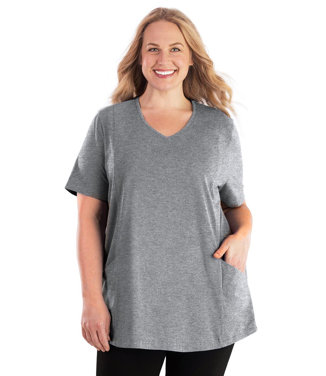 Plus size woman, facing front, wearing JunoActive plus size Stretch Naturals Lite Pocketed V-Neck Short Sleeve Top in the color Heather Grey. Her left hand is in the shirt pocket by her hip, her right arm is naturally at her side. She is wearing JunoActive Plus Size Leggings in the color Black. 