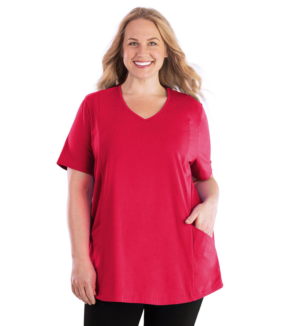 Plus size woman, facing front, wearing JunoActive plus size Stretch Naturals Lite Pocketed V-Neck Short Sleeve Top in the color Rosette. Her left hand is in the shirt pocket by her hip, her right arm is naturally at her side. She is wearing JunoActive Plus Size Leggings in the color Black. 