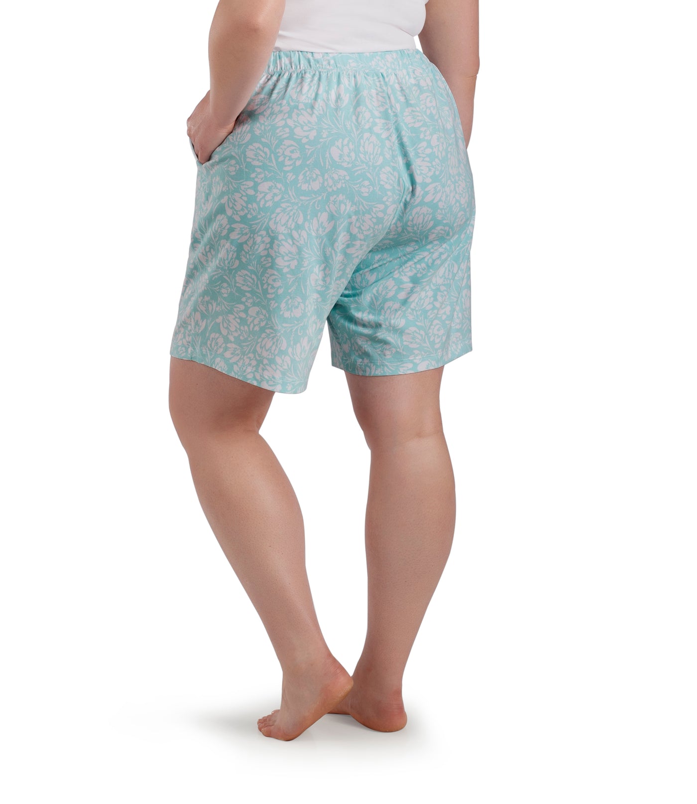 Bottom half of plus sized woman, facing back, wearing JunoActive JunoBliss Pocketed Sleep Shorts Spring Blue Floral Print. These shorts are longer and hemline comes to a few inches above knees and have pockets on both sides.