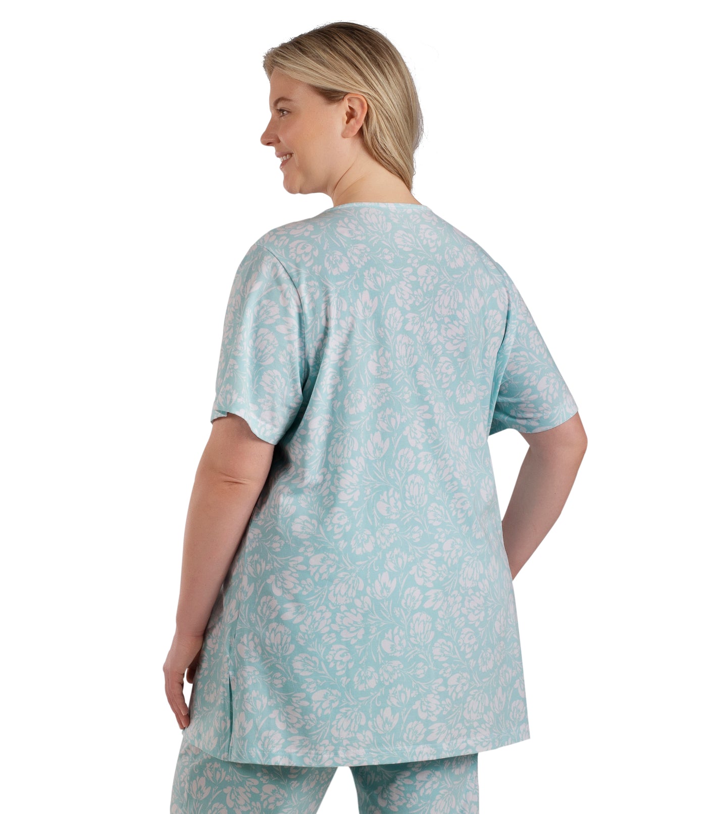 Plus size woman, facing back side profile, wearing JunoActive plus size JunoBliss V-Neck Short Sleeve Sleep Top in color Spring Blue Floral Print. The woman is wearing a pair of JunoBliss Pocketed Sleep Pants in color Spring Blue Floral Print.