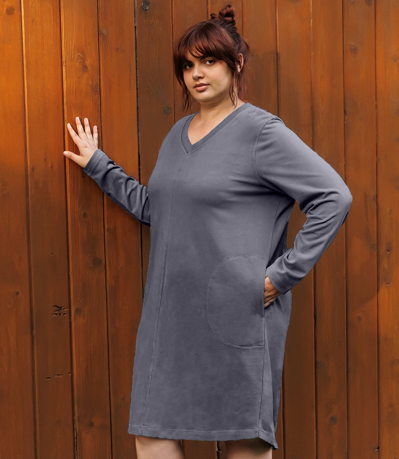 Plus-size model, facing forward, right hand on wall, left hand in dress pocket. Wearing JunoActive's Legacy Cotton Casual Pocketed Long Sleeve Dress in Misty Grey.
