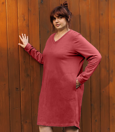 Plus-size model, facing forward, right hand on wall, left hand in dress pocket. Wearing JunoActive's Legacy Cotton Casual Pocketed Long Sleeve Dress in Sedona Red.